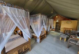 Spacious safari tent with wooden four-poster beds draped in white mosquito nets, zebra-print seating, rugs and wooden furniture.