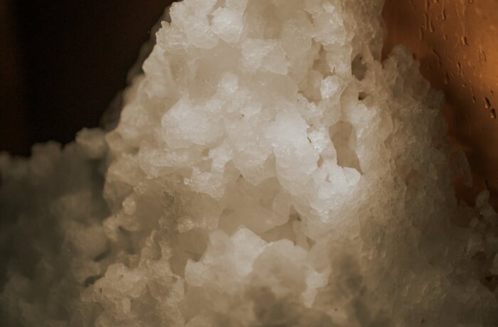 Crushed ice piled in a warm-lit copper bin, ready for cocktails or spa cold therapy with beaded condensation on the side.