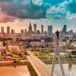 Panoramiczny widok miasta z mostem wantowym nad rzeką, nowoczesnymi wieżowcami i historyczną wieżą przy zachodzie słońca