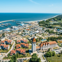 Hotel nad morzem z wieżą, budynki z czerwonymi dachami, marina z łodziami i falochronem, piaszczysta plaża, długa mierzeja, park rozrywki i baseny.