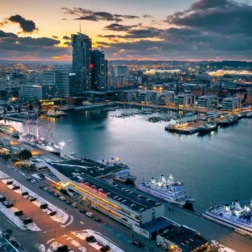 Port miejski o zmierzchu z oświetloną mariną, cumującymi promami, wysoką zabudową nad wodą, zaśnieżonym bulwarem i panoramą miasta