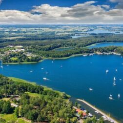 Widok z lotu ptaka na błękitne jezioro z żaglówkami, zalesionymi wyspami, mariną i nadbrzeżnym resortem — idealne na rejsy i relaks.
