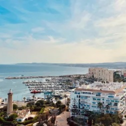 Coastal hotel panorama with marina, yachts, lighthouse and beachfront buildings overlooking Mediterranean sea and harbor