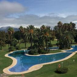Piscina all'aperto a forma di laguna con isola di palme, prati per prendere il sole e vista sulle montagne vicino alle ville dell'hotel.