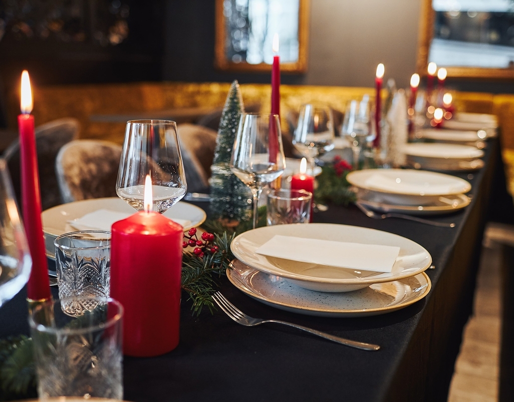 Festive dining table with red candles, wine glasses, stacked plates and greenery centerpiece in an intimate restaurant.
