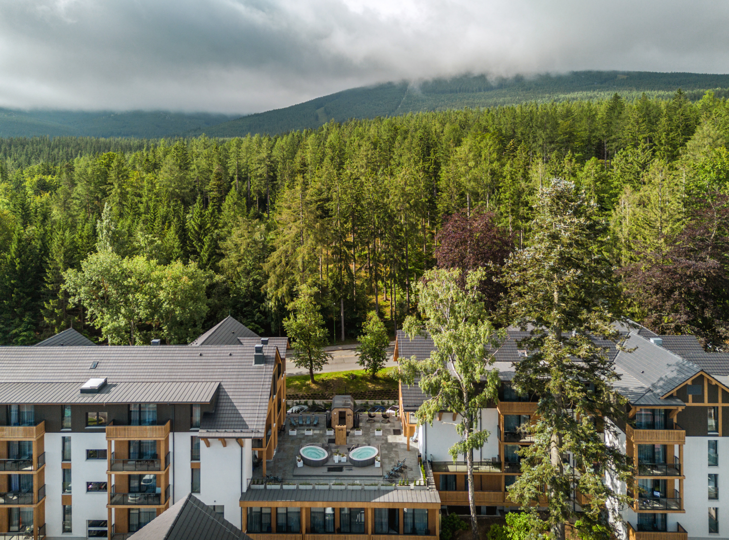 Fjällhotell med träbalkonger, takterrass med två runda bubbelbad och loungemöbler, omgiven av tät barrskog