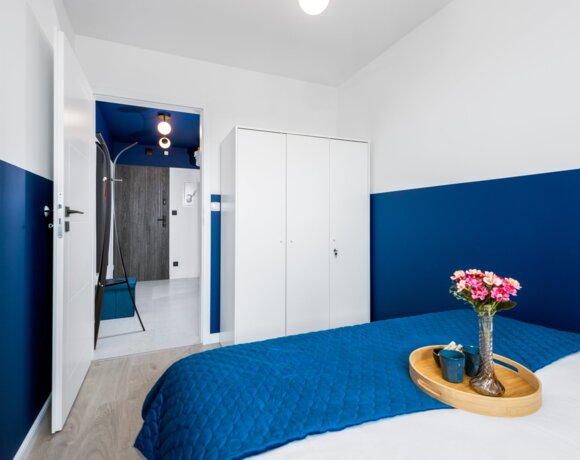 Modern hotel room with blue walls and bedding, white wardrobe, and a clean hallway with wooden entrance door