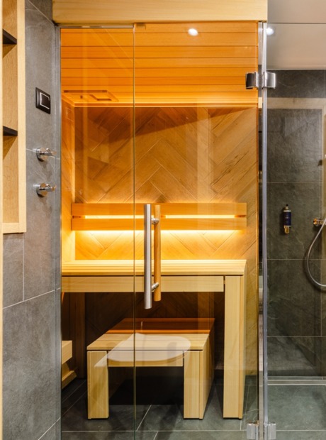 Private Sauna im Zimmer mit warmen Holzbänken hinter Glas, daneben moderne Duschkabine und Waschtisch