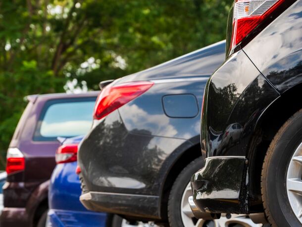 Parking hotelowy na terenie obiektu z zaparkowanymi samochodami w wyznaczonych miejscach pod drzewami