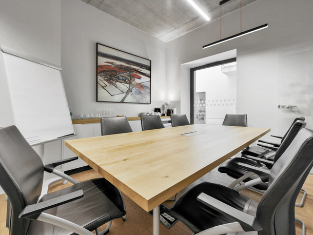 Nowoczesna sala konferencyjna hotelu z długim dębowym stołem, skórzanymi krzesłami, flipchartem i stacją kawową.