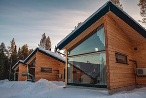 Chalés de madera en invierno con grandes ventanas panorámicas, tejados nevados, pinos y unidad exterior visible
